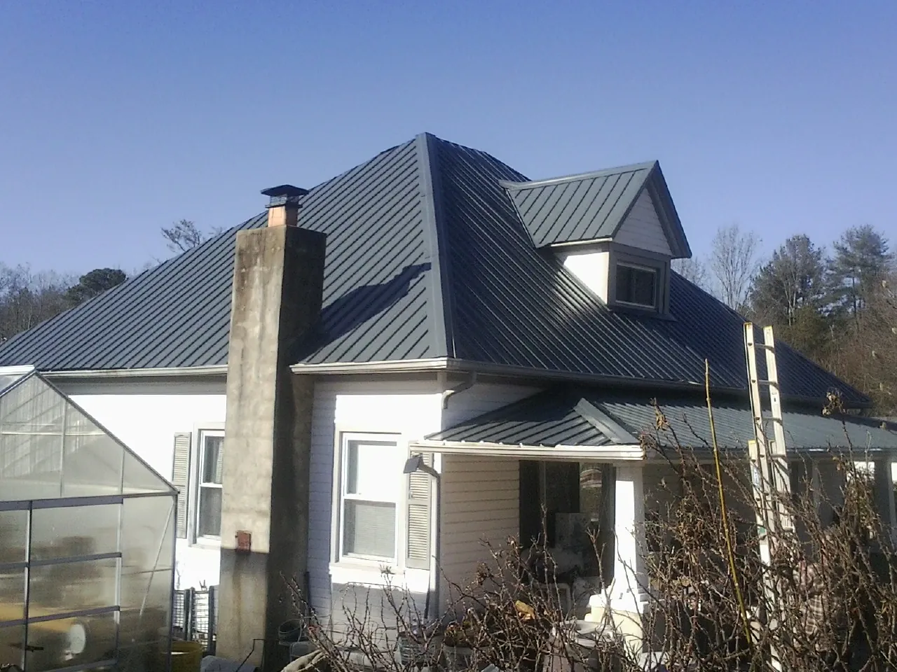 Dark blue standing seam metal roof on a white farmhouse with dormer — Slate & Tile Roof Repair by Roofing Brothers in Balsam