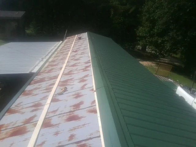 Old rusted panels beside newly installed green metal roofing — Wind Damage Roof Repair by Roofing Brothers in Balsam