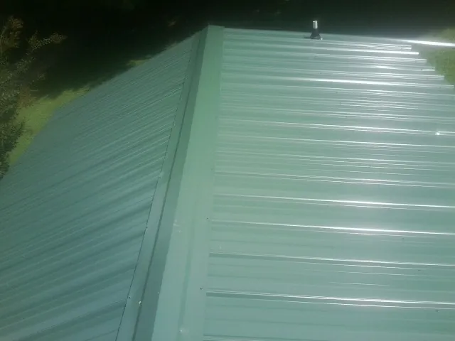 New green metal panels meeting at the ridge of a roof — Flat Roof Repair work by our crew in Balsam