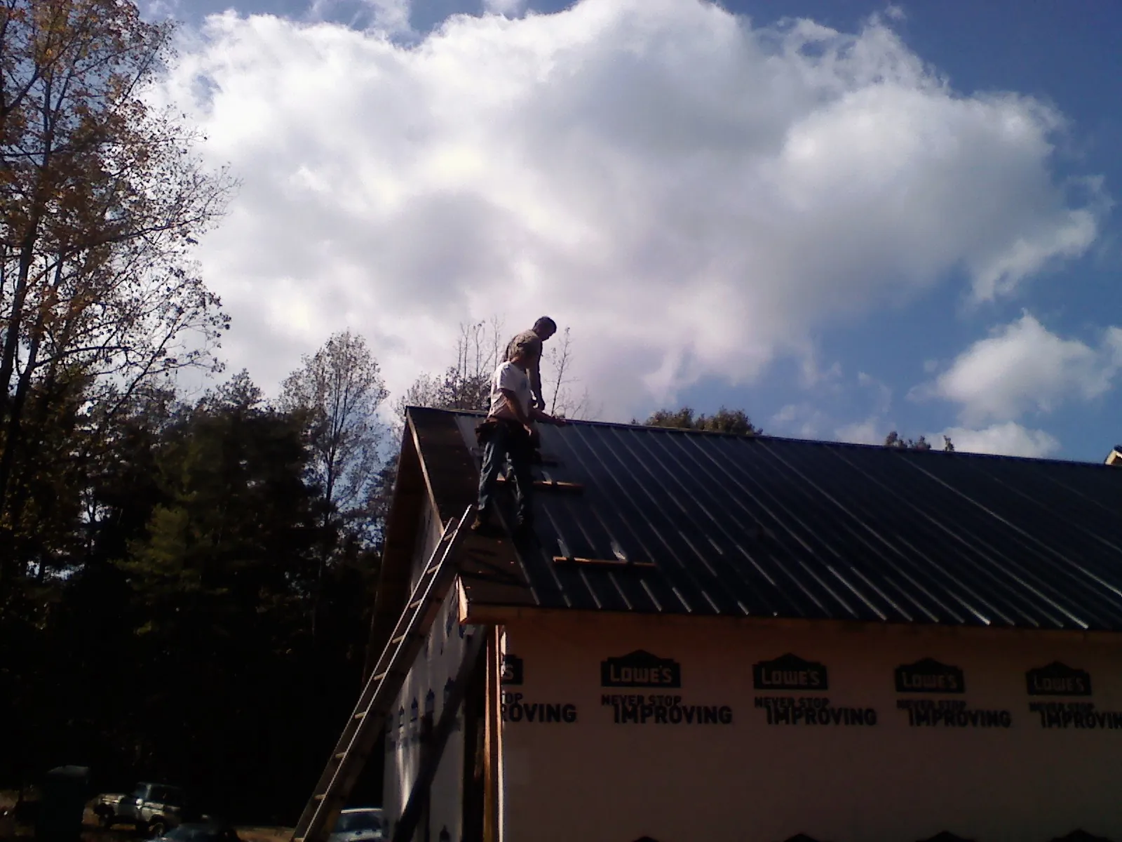 Roofer fastening dark metal panels high against a cloudy sky, from a Roof Inspection job in Balsam