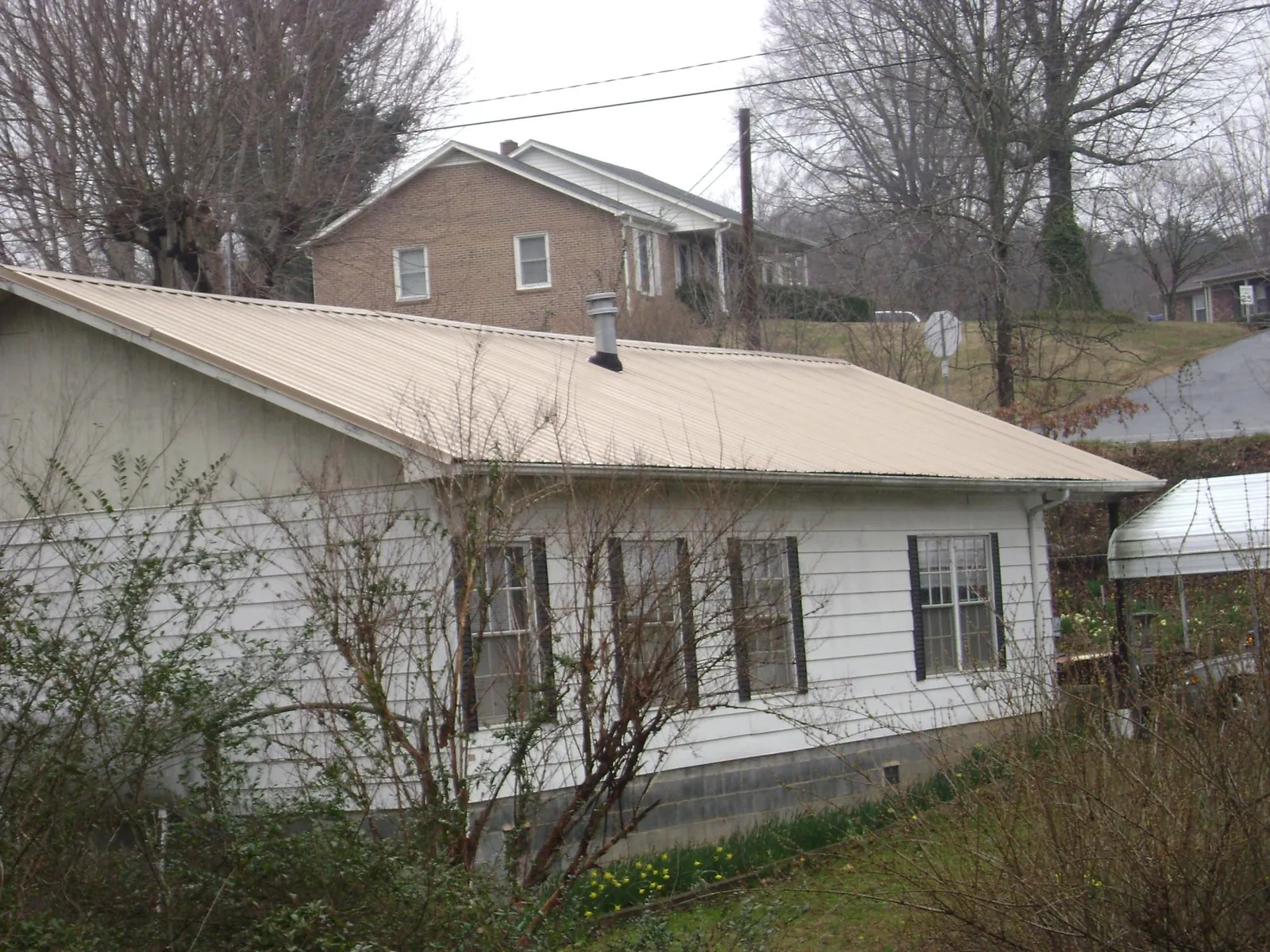 Tan metal roof on a white sided house set into a hillside — Commercial Roofing by Roofing Brothers in Balsam