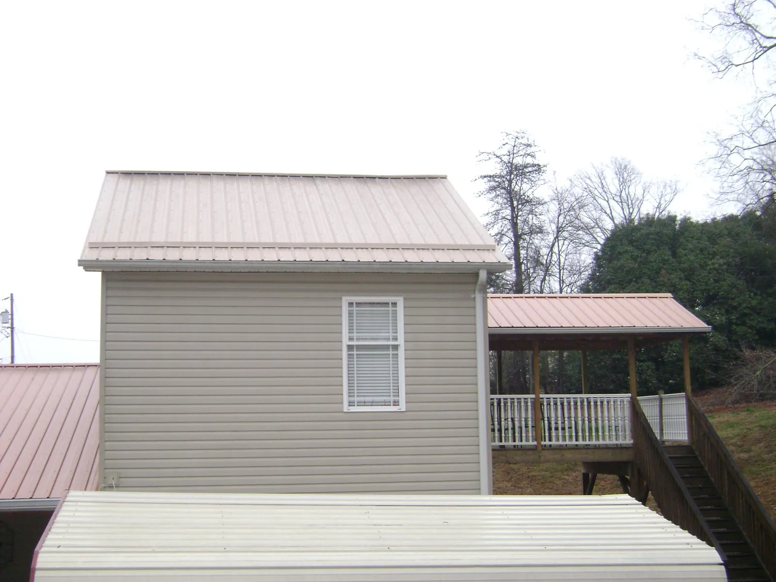 Tan metal roofs on a two story addition and attached porch, from a Roof Replacement job in Balsam
